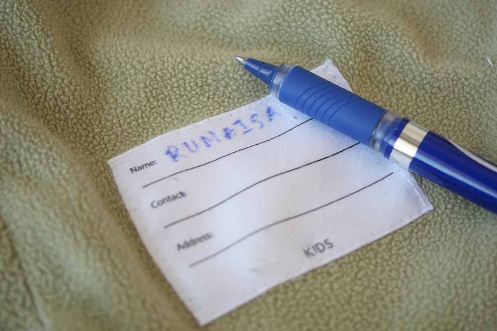 A blue pen rests next to a name tag for a child on a soft fabric.